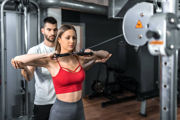 Young woman working with a fitness instructor on a weightlifting machine shoulder cable exercise ripl fitness