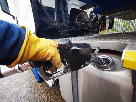 Semi Truck Being Refuelled with Diesel Close up with the Gloved Hand of the Truck Driver Holding the Fuel Nozzle and holding it in Place as He Fills up the Tank.