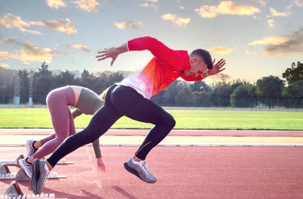 seorang pria dan seorang wanita meninggalkan blok awal di lintasan atletik. - lari 100 meter foto potret stok, foto, & gambar bebas royalti