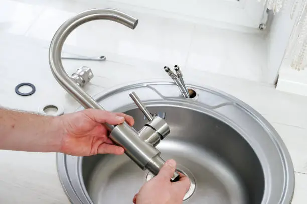 Photo of Plumber hand holds a new faucet for installing into the kitchen sink
