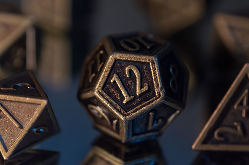 A close-up image of a 12-sided rpg die on a reflective surface with in the background the other dice of the set.