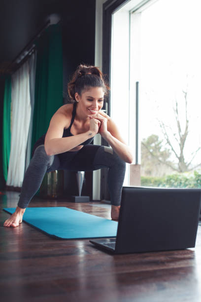 istock Young woman doing squat exercise from online tutorial with toothy smile at home 1306018919