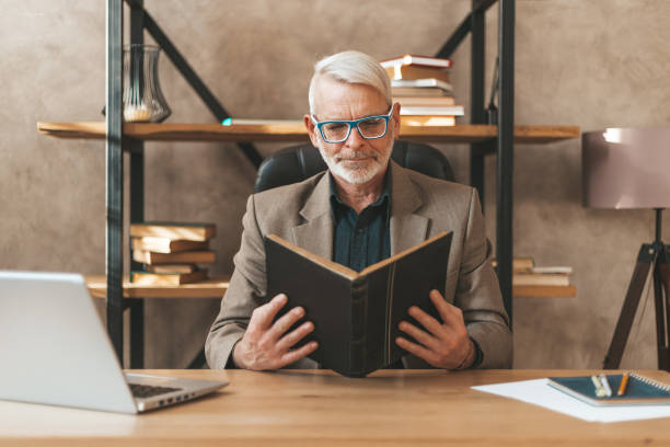 istock Reading in the home library. An elderly man is reading a book at the table, a hobby and a quiet leisure time in retirement 1306024154