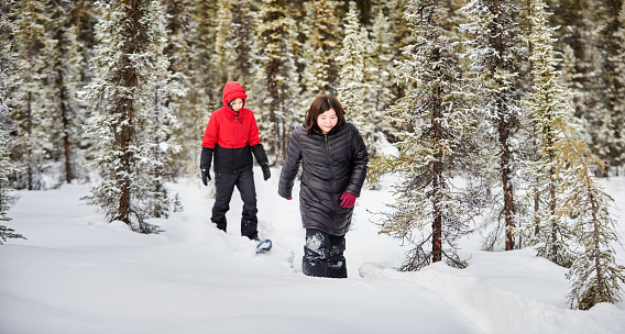Girls wearing warm clothes and snowshoes walking through snow in forest
