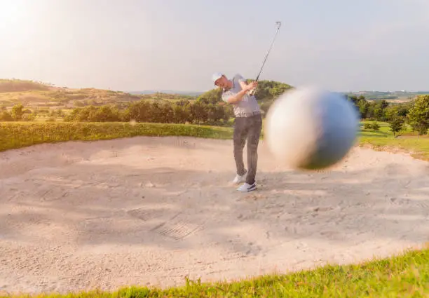 Male golfer shoting golf ball from sand bunker. Handsome asian golfer hitting golf ball with sand blast.