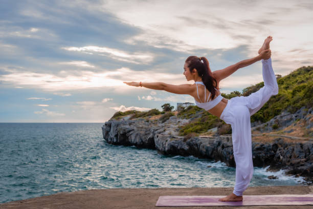 beautiful asian woman is practicing yoga on the asana in outdoors with sea and sky - stretch beach imagens e fotografias de stock