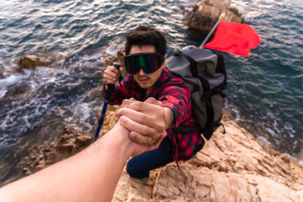 Man giving helping to friend by hand pull while climb mountain rock cliff.