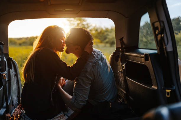 Kiss under perfect sunset Romantic young couple sitting and kissing in open car trunk, enjoying sunset in spring nature while taking a break from long road trip kissing stock pictures, royalty-free photos & images