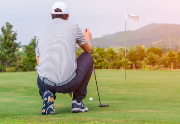 golfista masculino arrodillado sosteniendo palo de golf y comprobando línea de ruta - putting fotografías e imágenes de stock