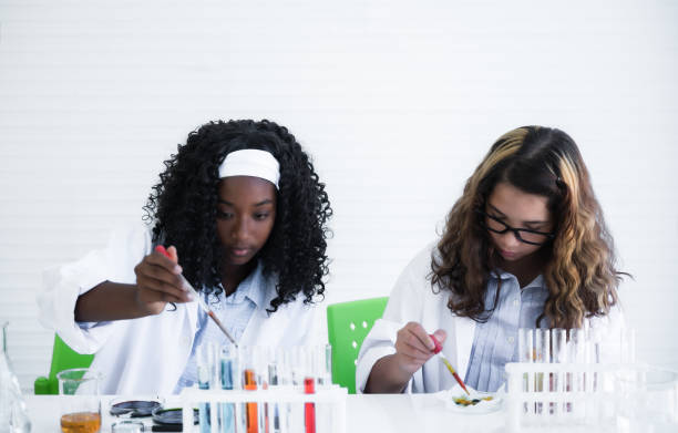 felice studente africano e caucasico con pelle diversa sta imparando e testando la sostanza chimica scientifica con liquido colorato in becher e provetta in laboratorio. - laboratory test tube student scientist foto e immagini stock