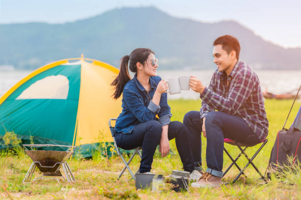 azjatycka młoda para siedząca pijąc kawę szczęśliwie w pobliżu jeziora i obozu namiotowego - camping hiking tent couple zdjęcia i obrazy z banku zdjęć