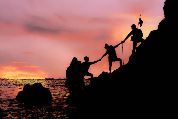 istock Silhouette of climbing team helping each by hand pull while climb mountain rock cliff 1306028416
