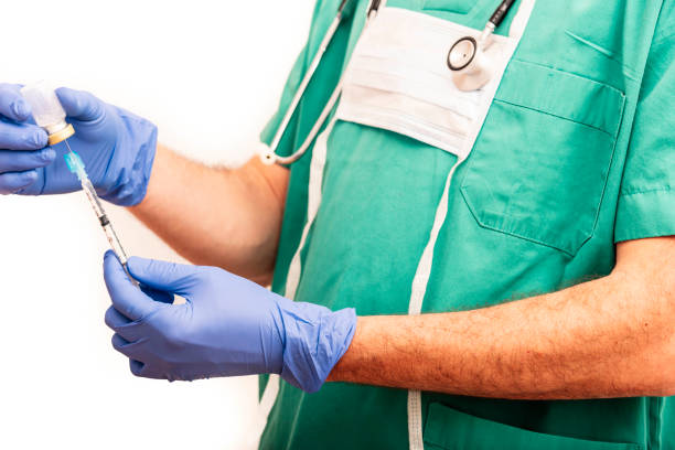 infirmière mâle portant le vaccin ou le médicament dans la seringue avec l’aiguille de sûreté, rectifiée dans les gommages verts sur le fond blanc. - biotechnology student laboratory nurse photos et images de collection