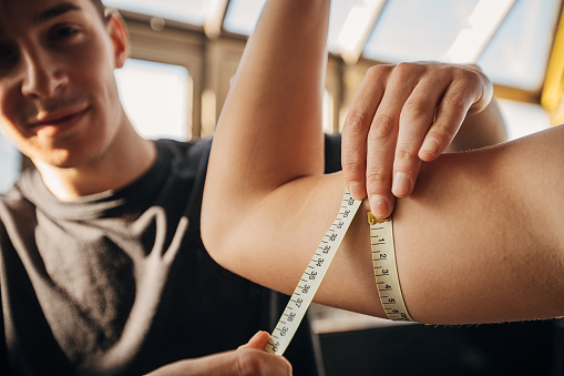 Two people, male personal trainer measuring woman's bicep in gym.