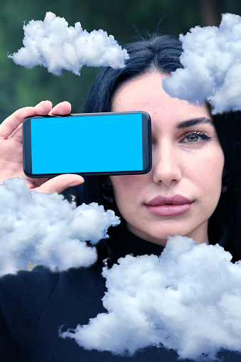 Portrait of a long black hair caucasian young woman holding mobile phone and showing empty screen of phone