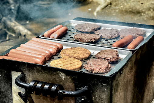 Horizontal shot of burgers and hot dogs cooking on an outdoor grill.