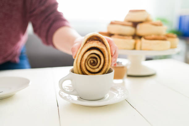 Caucasian woman dipping a delicious cinnamon roll in her hot coffee cup. Woman with a sweet craving eating a cinnamon roll for breakfast in the morning