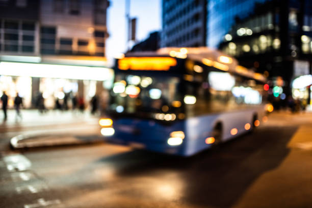 A green bus drives through a city at night, illuminated by streetlights. The city buildings and other vehicles are blurred in the motion of the bus.