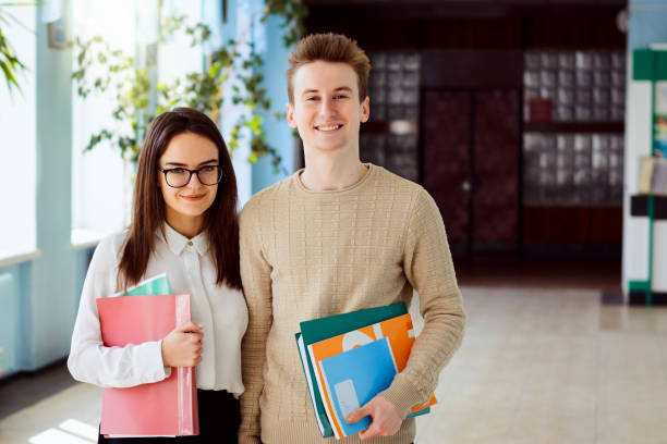 istock Portrait of two high-school learners with course books, text-books and folders before classes in school corridor in sunny day 1306046631