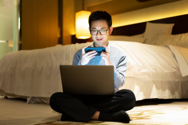 istock Asian man taking a break with mobile games while working beside the bed with laptop at night 1306050082
