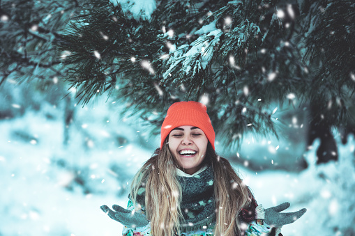 Portrait of young beautiful woman enjoying the snowfall and smiling and wearing thick clothes outside in cold weather