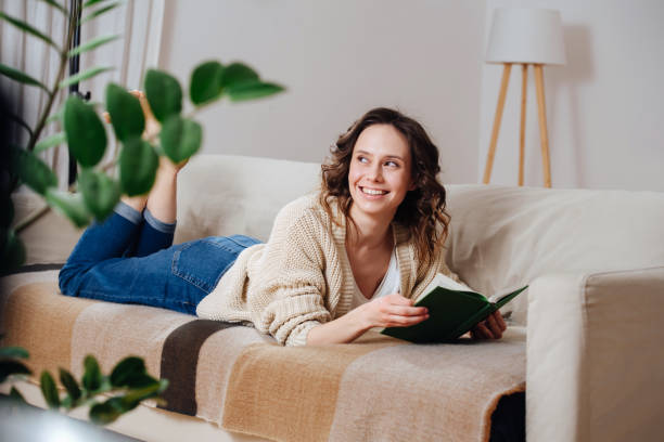 istock Smiling young woman lying on a couch with a book, looking at someone 1306051139