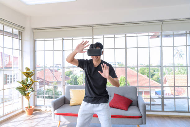 istock Young Asian man getting experience with VR virtual reality headset or 3D glasses in living room at home. technology, gaming, entertainment concept 1306052301
