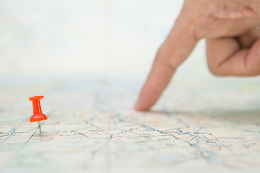 Selective focus of Red pin and blurred fingers pointing on the map  background