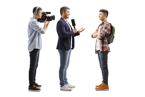 Full length profile shot of a reporter with a microphone and a cameraman interviewing a male student isolated on white background