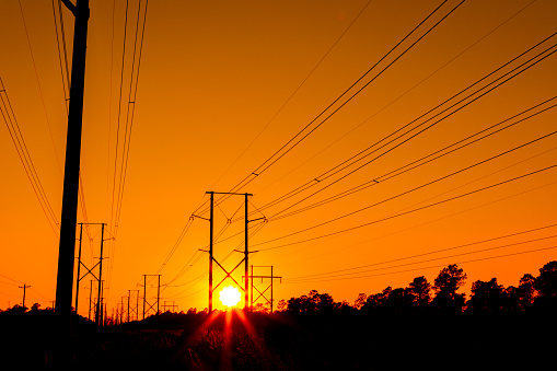 The sun sets behind distant high voltage electrical lines with orange sky.