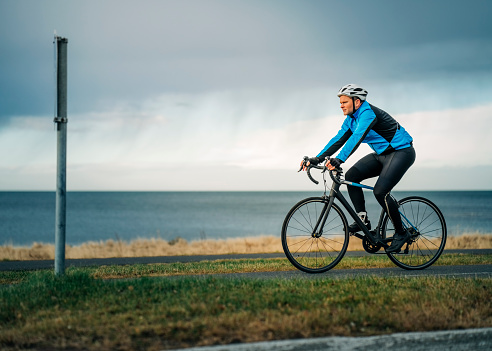 Side view of a male cyclist in fitness wear and helmet riding his bike on the road along the beach. Bicycle rider riding his cycle on road along the beach.