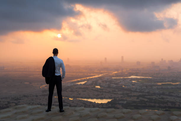 Photo of Businessman standing on top of a high-rise rooftop looking at the city view at sunset.