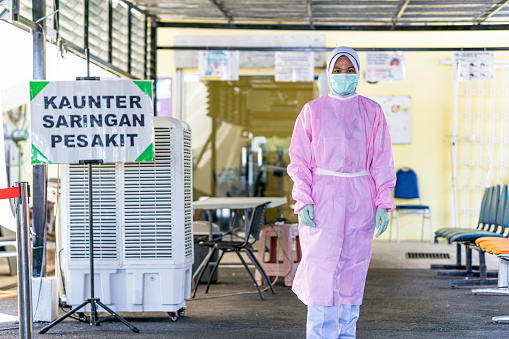 Female frontliner in Malaysia performing her tasks during the coronavirus pandemic while wearing full PPE standing beside a signboard 'triage counter for patients'