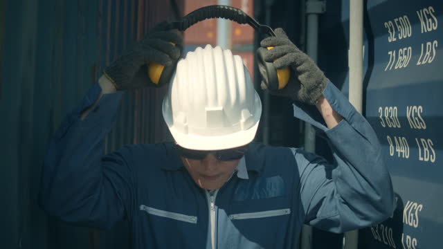 Male worker putting on safety ear muffs to prepare before work in shipping port,Slow motion