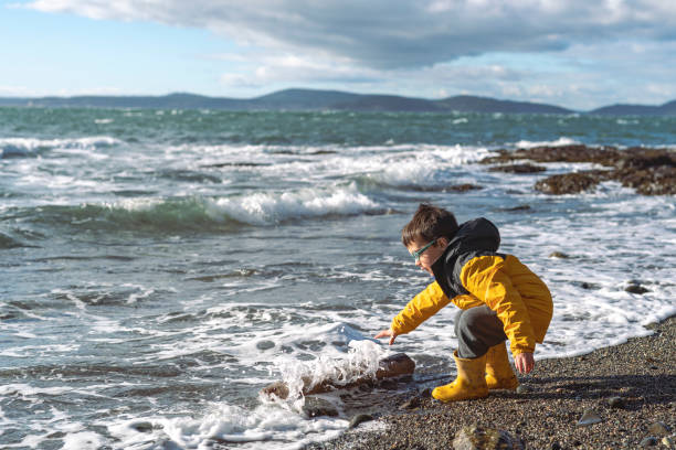 istock Young five-year old boy playing on a beach and watching the waves crash on the shore 1306074784
