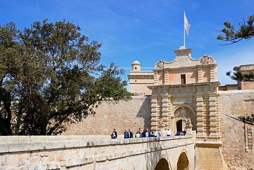 Tourists crossing the footbridge leading to the Town Gate and city centre, Mdina, Malta, Europe.