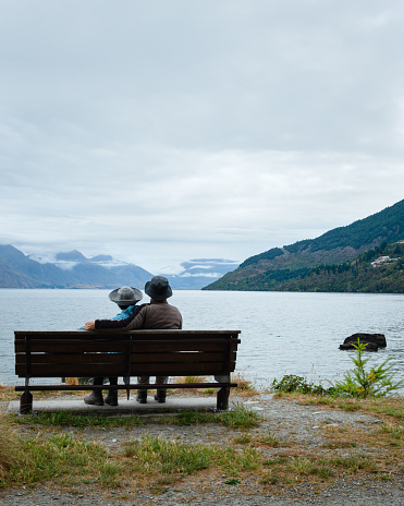 A couple sitting on the bench, enjoying the views of Lake Wakatipu and mountain ranges of Queenstown. Vertical format.