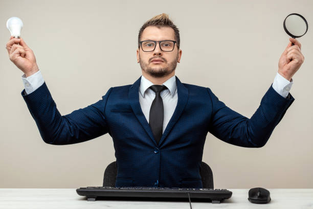 istock A businessman in a blue suit at a work table. Holds a magnifying glass and a light bulb. Effective business work concept. 1306079950