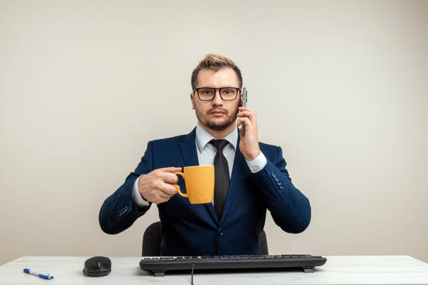 istock A businessman in a blue suit at a work table. Holds a mug and a phone. Emotional work. Multitasking, effective business worker concept. 1306079957