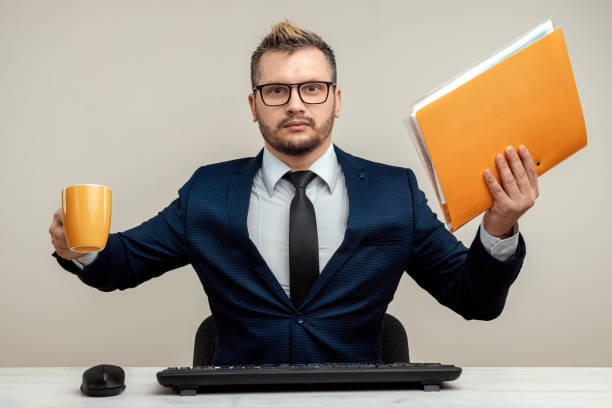 istock A businessman in a blue suit at a work table. Holds a folder with documents and a mug in his hands. Effective business work concept. 1306079962