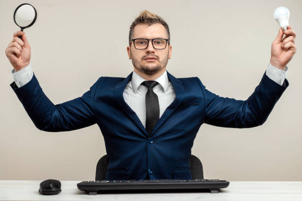 istock A businessman in a blue suit at a work table. Holds a magnifying glass and a light bulb. Effective business work concept. 1306079963