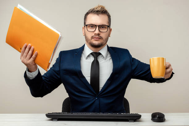 istock A businessman in a blue suit at a work table. Holds a folder with documents and a mug in his hands. Effective business work concept. 1306079964
