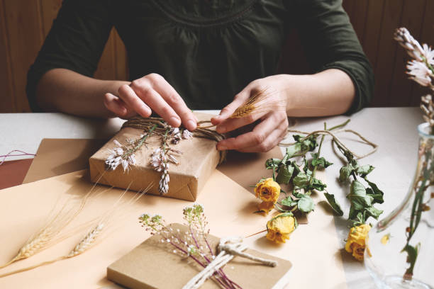 istock Woman makes zero waste, plastic free, trendy hand made gift package with craft recycled paper and dried flowers on the table with linen tablecloth. Natural aestetic. 1306089264