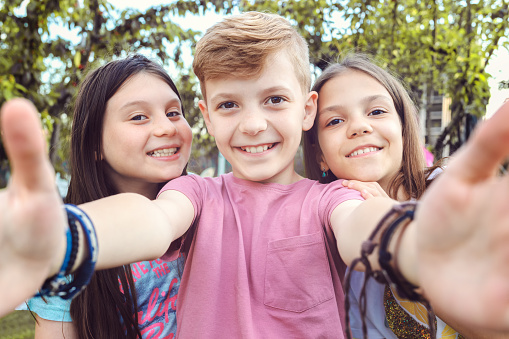 Best friends taking selfie outdoors in backyard – happy friendship with smart kids having fun celebrating summer vacation – modern children enjoying time together at garden party playing and smiling