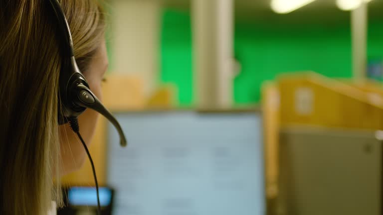 Rear view female Call center worker in headset talking on the phone and answering of questions. Service phone operator in earphones helping customers in business office. Slow motion shot.