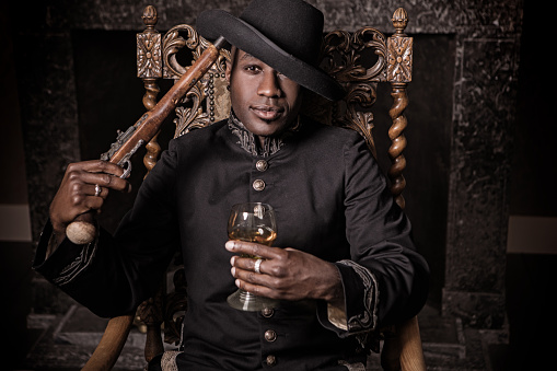 Handsome traditional dutch black man wearing historically correct outfit holding a gun in a typical townhouse drawing room
