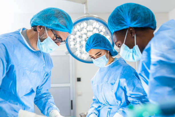 urgent surgery. professional smart intelligent surgeons standing near the patient and performing an operation while saving his life - cirurgião imagens e fotografias de stock