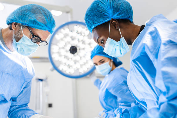 team of professional doctors performing operation in surgery room. medical team performing surgical operation in bright modern operating room - urgency body care young adult people imagens e fotografias de stock