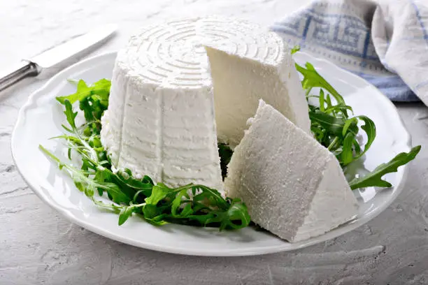 Photo of Ricotta cheese and arugula on white plaster background.