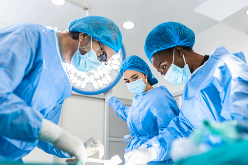 Preparation for the beginning of surgical operation with a cut. Group of surgeons at work in operating theater toned in blue. Medical team performing operation